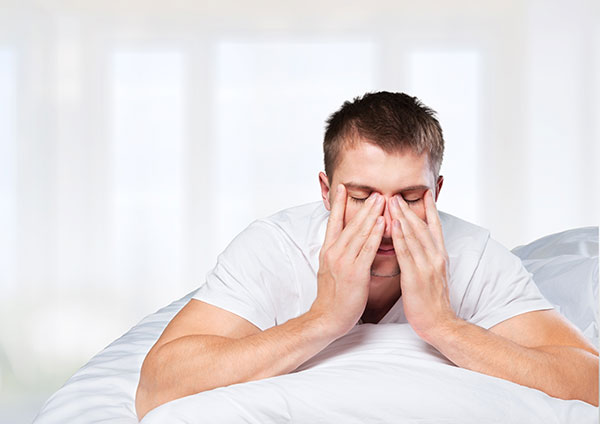 Man sitting on the edge of his bed looking exhausted, illustrating why you feel tired after sleeping 8 hours but still tired
